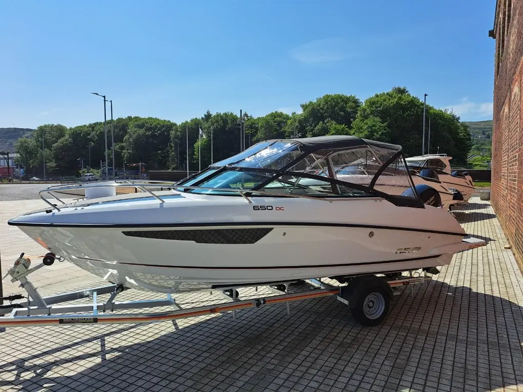 A sleek white boat on a trailer, labelled '650 DC', parked by a brick wall under clear blue skies.